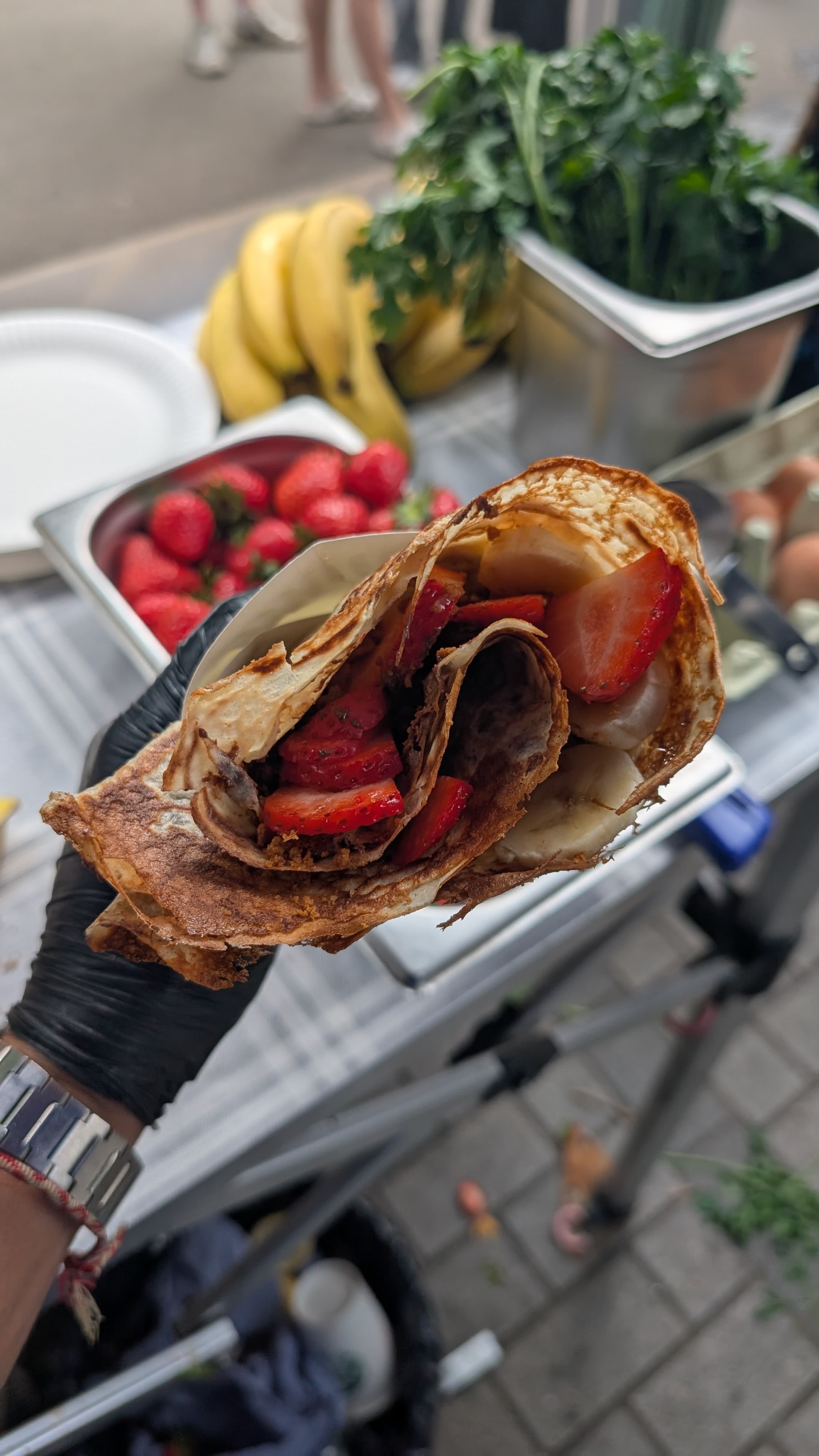 Sweet crêpe wrap held in a gloved hand, fresh strawberries spilling from the fold