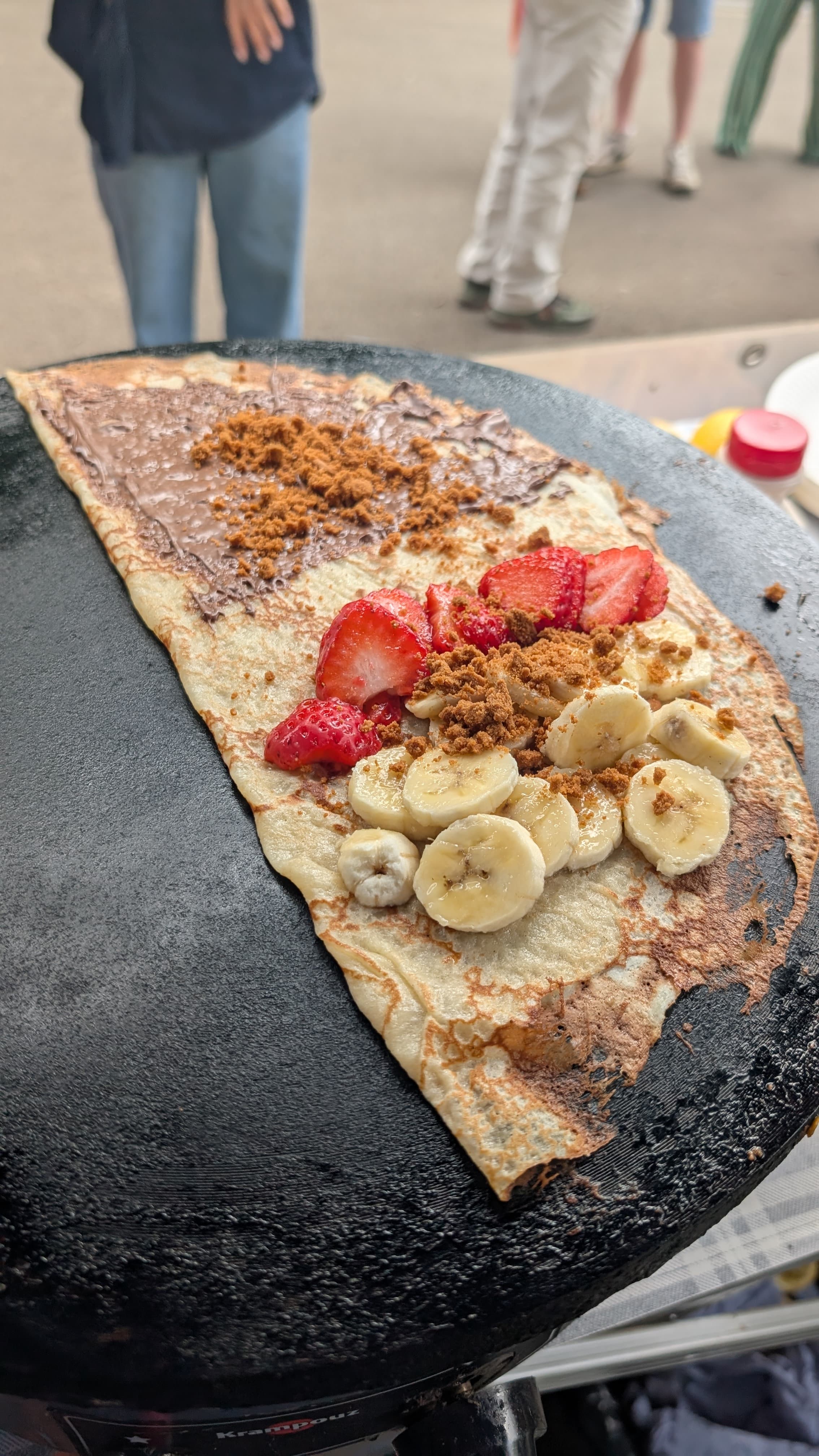 Top-down view of a sweet crêpe topped with Nutella, fresh strawberries, banana rounds and speculoos crumb